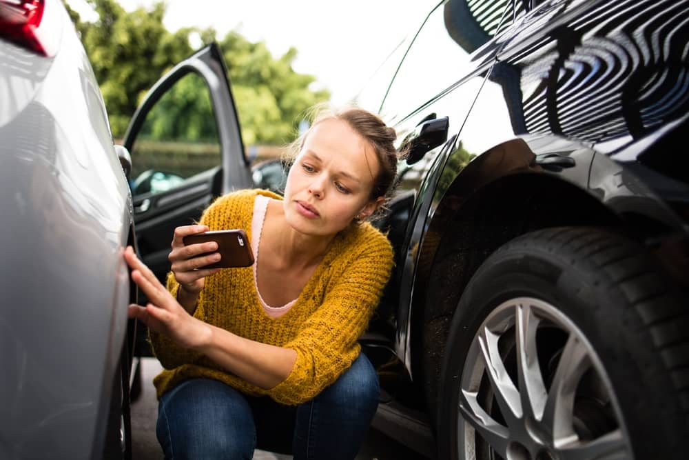 Woman taking a picture of a car scratch after and accident