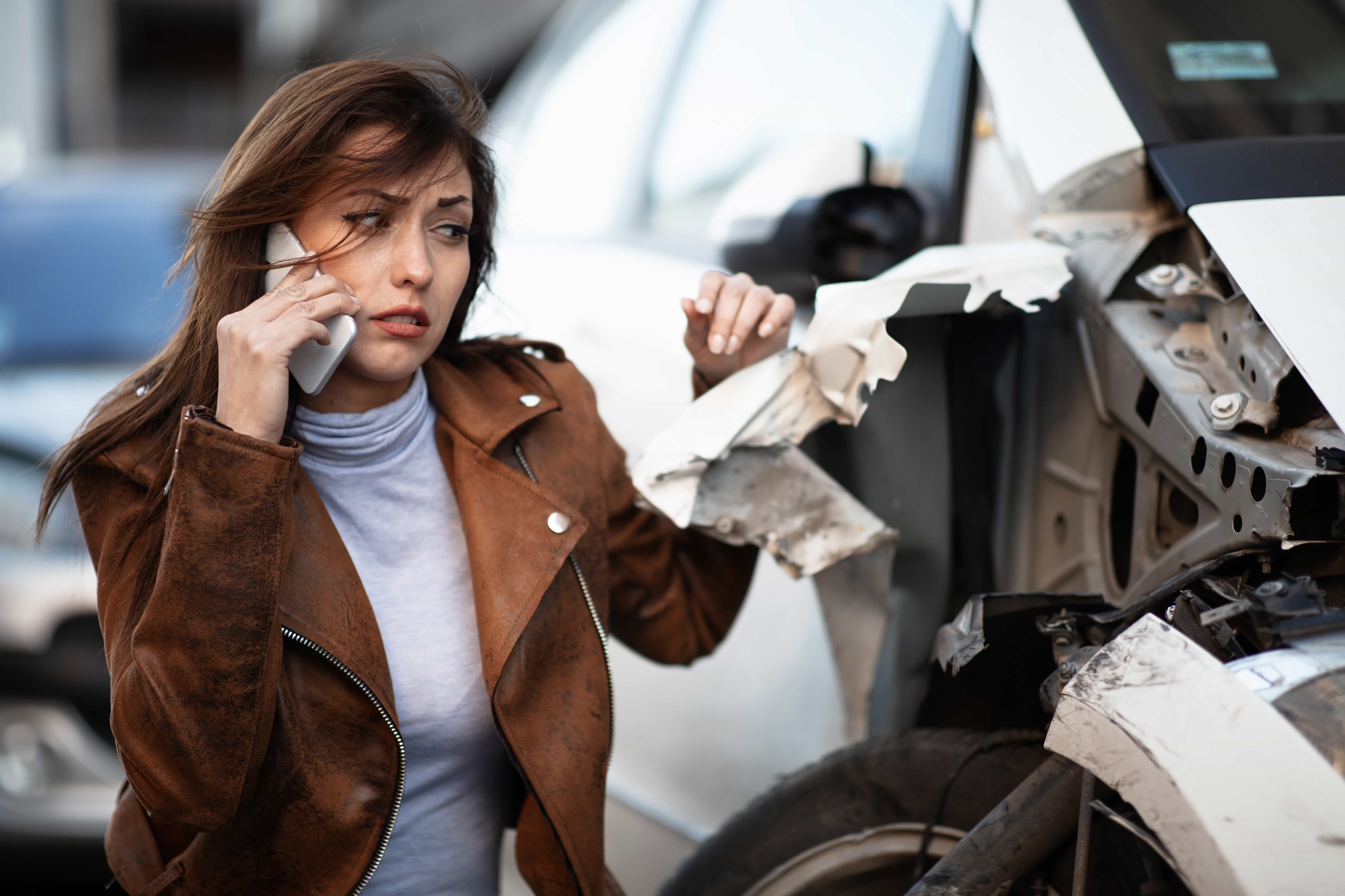Mujer hablando por teléfono junto a un vehículo dañado tras un accidente de auto en Colorado